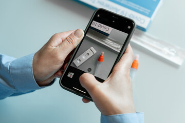 Female hands making photo shot of self testing kit with positive covid 19 result with a phoner...