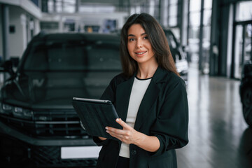 Wireless device, holding digital tablet. Saleswoman in car showroom, selling automobile