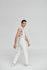 A man in a white sleeveless shirt and pants poses confidently against a white backdrop.