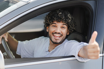 Excited Indian man is sitting in his new car and showing thumb up