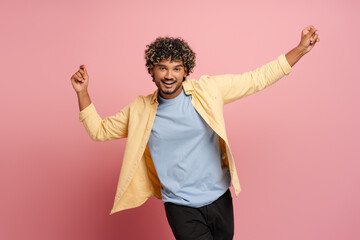 Cheerful Indian young man is dancing and having fun on pink background