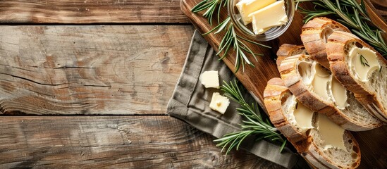 Rustic wooden board featuring fresh bread slices butter and rosemary on a soft background with copy space image