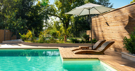 Swimming pool in modern private villa with lounge chairs, palm trees and umbrella