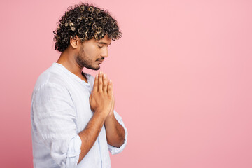 Attractive, pensive man praying with hope on pink background