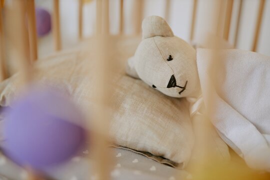 Medium close up of cute plush bear under white sleeve blanket in baby cot