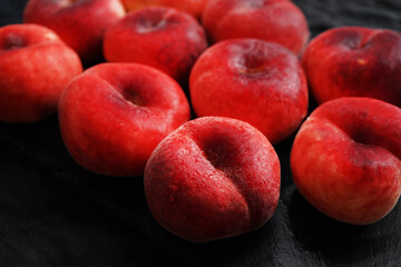 Ripe flat peaches on a black tray on a dark background