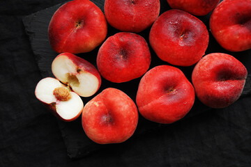 Ripe flat peaches on a black tray on a dark background