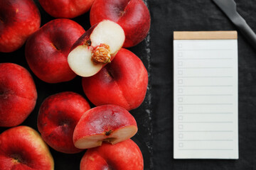 Ripe flat peaches on a black tray next to a to-do list on a dark background