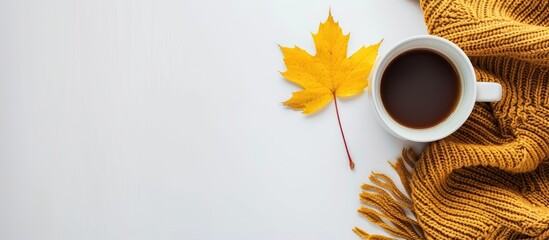 A fall themed setup with a cup of coffee cozy sweater and a yellow maple leaf on a white backdrop providing a blank area for text. Creative banner. Copyspace image
