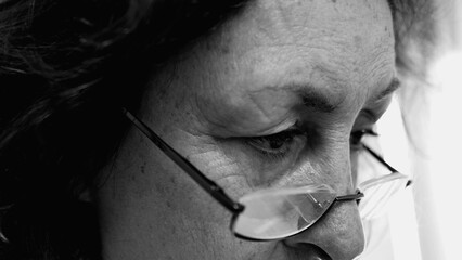 Black and white close-up of an elderly woman's focused eyes wearing glasses, deeply engaged in...