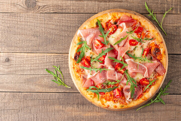 Pizza with prosciutto, ham, arugula, spinach, tomatoes, pesto, cheese and parmesan. Italian cuisine
