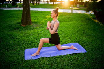 Concentrated alone fitness slim young woman doing stretching and yoga exercises on mat in park at sunset, wellbeing and healthy sportive lifestyle