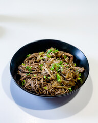 Buckwheat soba noodles with pork and sweet and sour sauce in a black plate on a white table