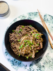 Buckwheat soba noodles with pork and sweet and sour sauce in a black plate on a white table