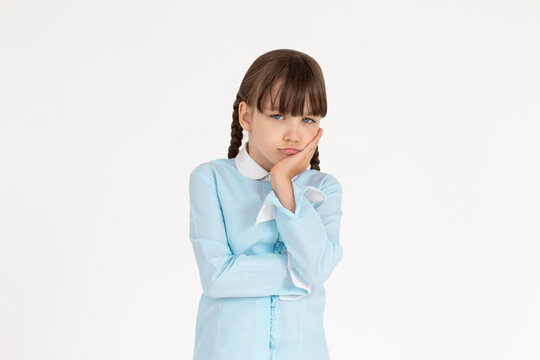 Cute school girl standing in uniform, holding palm on cheek and leaning face on it, being bored and tired of uninteresting talks, feeling indifferent to what happening over white wall