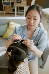 High angle shot of Asian mom doing her brunette daughter hair in nursery