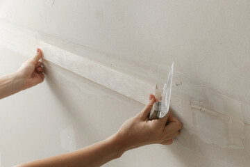 Woman taping and mudding joins pieces of drywall into a single solid wall. Fixing dry wall surface and preparation for painting. DIY housing improvement project.