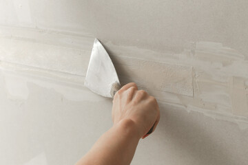 Woman taping and mudding joins pieces of drywall into a single solid wall. Fixing dry wall surface...