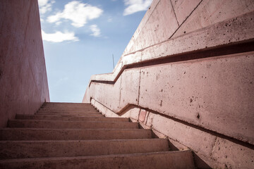  A dramatic black and white photograph of a concrete staircase viewed from below, leading upwards with the sky in the background, showcasing architectural details and geometric shapes.
