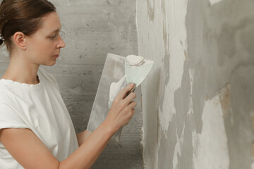 Woman plastering wall with putty-knife. Fixing wall surface and preparation for painting. DIY housing improvement project.