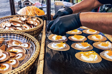 Vendor wear glove make Thai Crispy Pancake or Kanom Buang on gas stove pan. A traditional Thai dessert menu with crispy flour and foi thong filling. Thai Style Crisp Tart, A kind of filled pancake