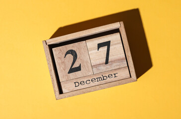 Wooden block calendar with the date december 27 on yellow background