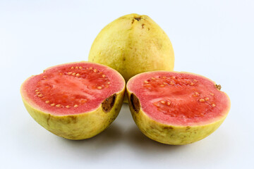 two red guavas, one of which is sliced ​​and the inside looks very ripe with a tempting reddish color against a white isolated background
