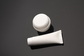 White jar and tube of cream on a black background