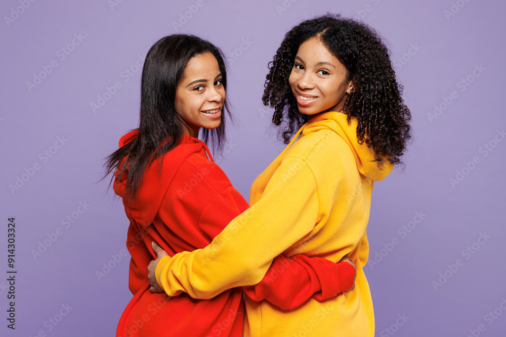 Wall mural Rear view of two young happy little kid teen girls women they wear red yellow hoodie casual clothes hug embrace put hands on back of each other isolated on plain purple background. Lifestyle concept.