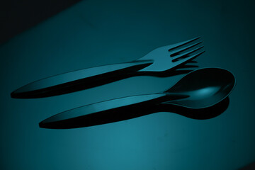 Black plastic spoon and fork in blue neon light