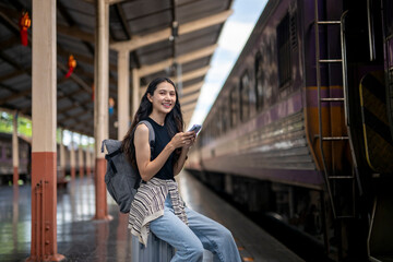 A woman is sitting on a train platform with a backpack and a cell phone