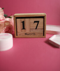 Wooden block calendar with the date March 17 and bouquet of roses, trays on pink background