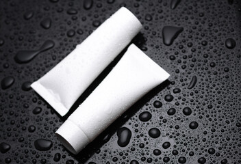 White cream tubes on a black background with water drops