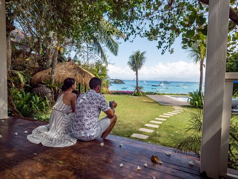 Couple enjoying a tropical beach view from a wooden deck.