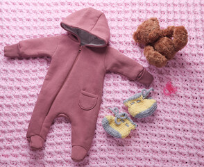 Overalls for newborn with shoes, toy bear and pacifier on blanket.