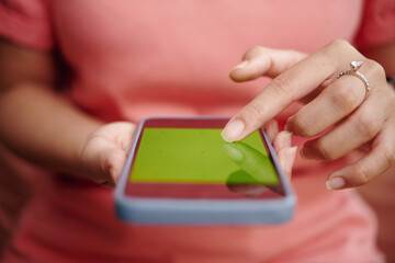 Close-up of hand wearing a ring tapping screen of smartphone with green chroma key background, focusing on action of interaction