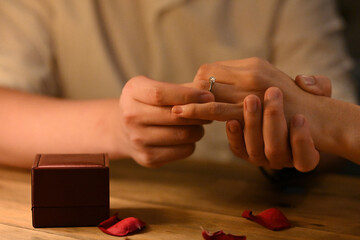 A close-up of the groom's hand places the engagement ring on the bride's hand, the essence of a...