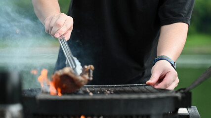 A person using tongs to lift a steak off the grill, with flames and smoke creating a dramatic backdrop, capturing the skill of grilling outdoors