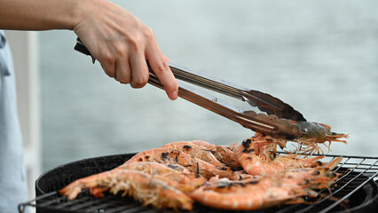 Using tongs to skillfully maneuver prawns on the grill, achieving a golden-brown crust while ensuring the meat inside remains tender and juicy
