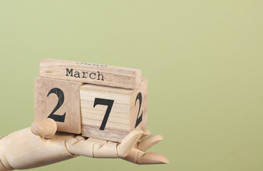 Wooden block calendar with date March 27 in the hand of puppet on green background