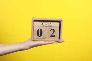 Wooden block calendar with date april 02 in hand on yellow background