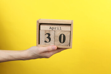 Wooden block calendar with date april 30 in hand on yellow background