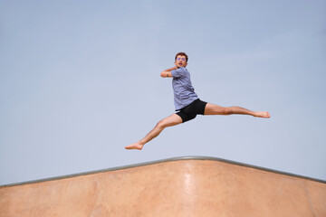 Fototapeta premium Young man is jumping gracefully in the air at a skate park, showcasing his athleticism and passion for movement