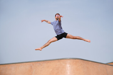 Dancer is performing a split jump over a skatepark ramp against a clear blue sky