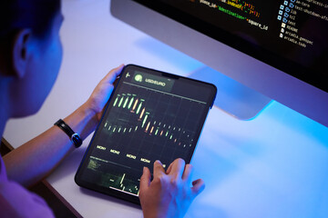 Person analyzing data on tablet with graphical interface displayed, coding display on monitor in...