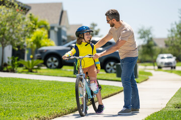 Happy Fathers day. Father and son in bike helmet for learning to ride bicycle at park. Father helping son cycling. Father and son on the bicycle on summer day. Kid son trying to ride bike with father.