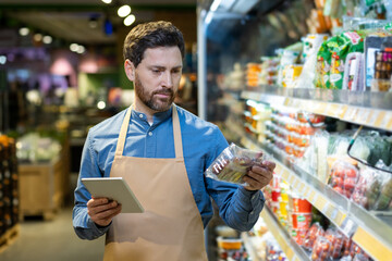 Grocery store worker holding tablet checking product on shelf in supermarket. Supermarket employee...