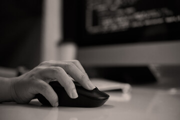 Close-up view of hand operating computer mouse on desk with monitor in background. Image focuses on...