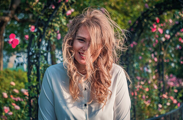 A young woman with curly hair enjoys a sunny day in a beautiful garden filled with blooming roses