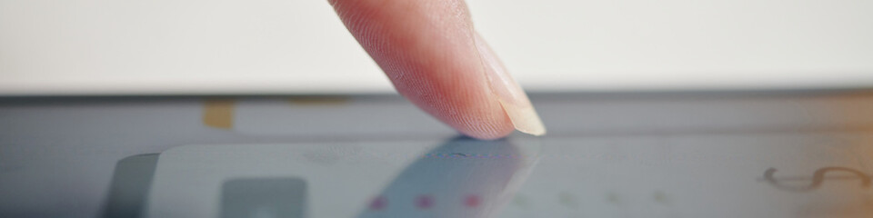Close-up of finger touching a tablet screen displaying faint graphics with reflections visible. Capturing the interaction with touchscreen technology in detail